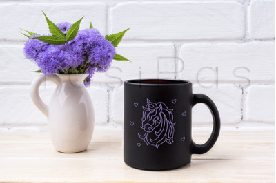 Black coffee mug mockup with blue Ageratum in pitcher