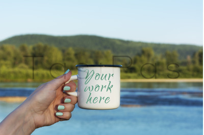 Woman holding enamel mug with river view.