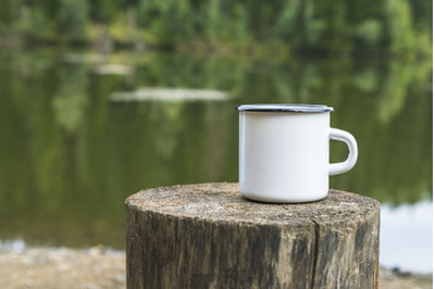 White enamel mug mockup with tree stump.