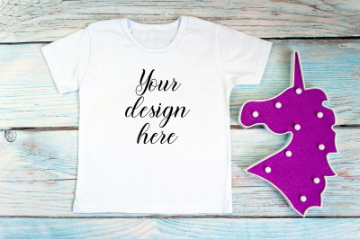 Kids White t-shirt mockup with unicorn toy on a wooden background.