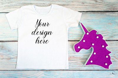 Kids White t-shirt mockup with unicorn toy on a wooden background.