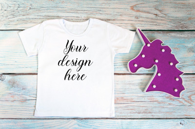 Kids White t-shirt mockup with unicorn toy on a wooden background.