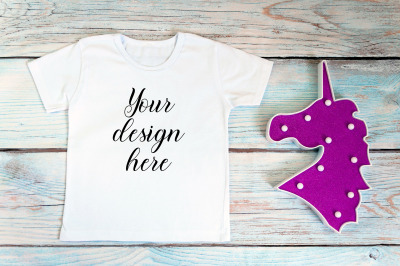 Kids White t-shirt mockup with unicorn toy on a wooden background.