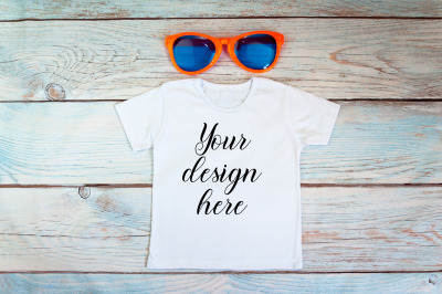 Kids T-shirt Mockup with sunglasses on a wooden background.