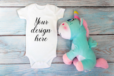 Baby Bodysuit mockup with unicorn toy on a wooden background.