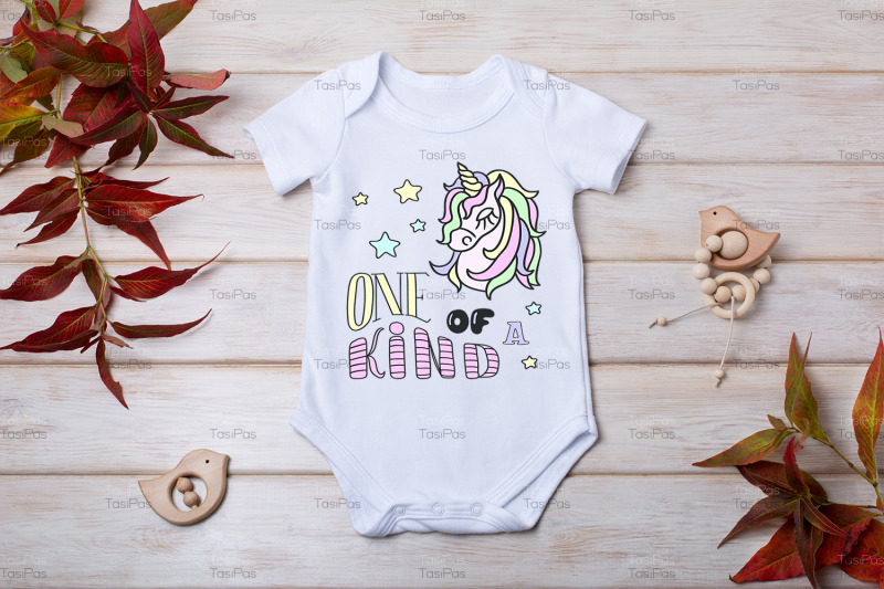 white-baby-short-sleeve-bodysuit-mockup-with-red-grass-and-baby-toys