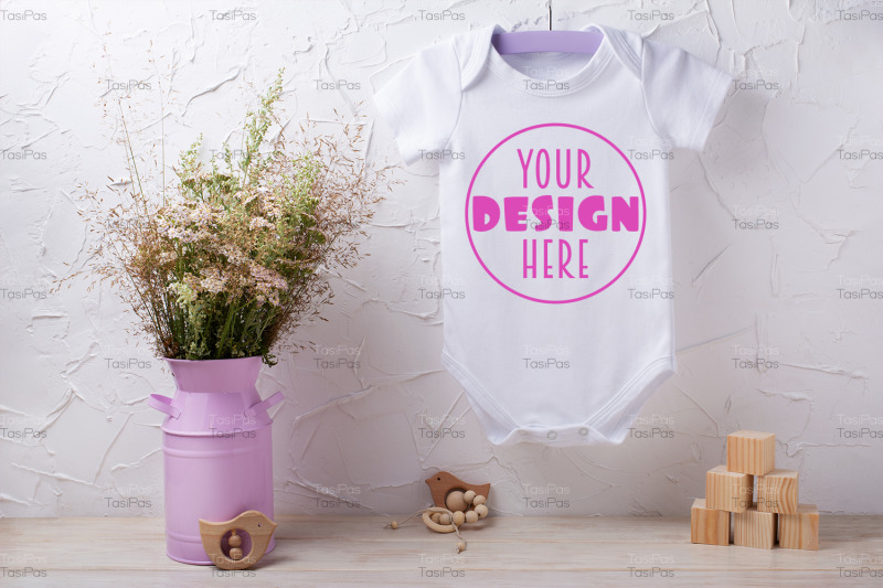 white-baby-short-sleeve-bodysuit-mockup-with-wild-flowers-and-wooden-c