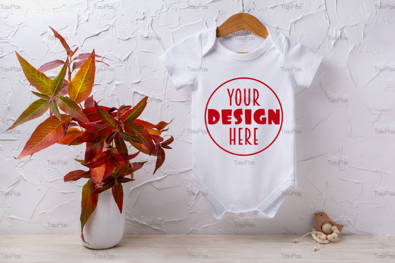 white-baby-short-sleeve-bodysuit-mockup-with-red-grass-and-wooden-toy